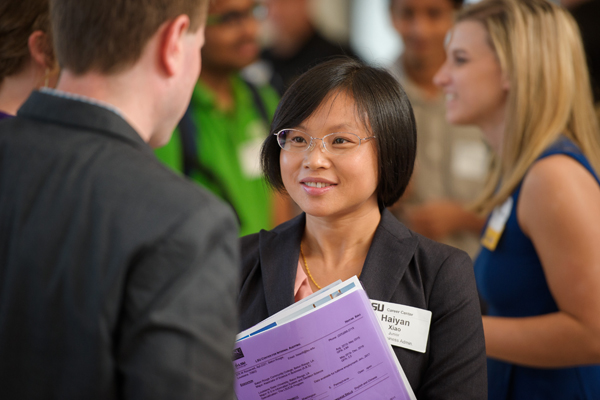 female in a suit holding a book while speaking to a man